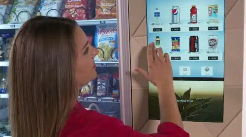 A woman selecting a product on a 22" digital touchscreen for a custom vending machine.