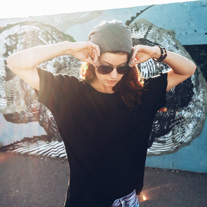 A female model adjusting her sunglasses in a hip urban alleyway to promote custom clothing vending machines.